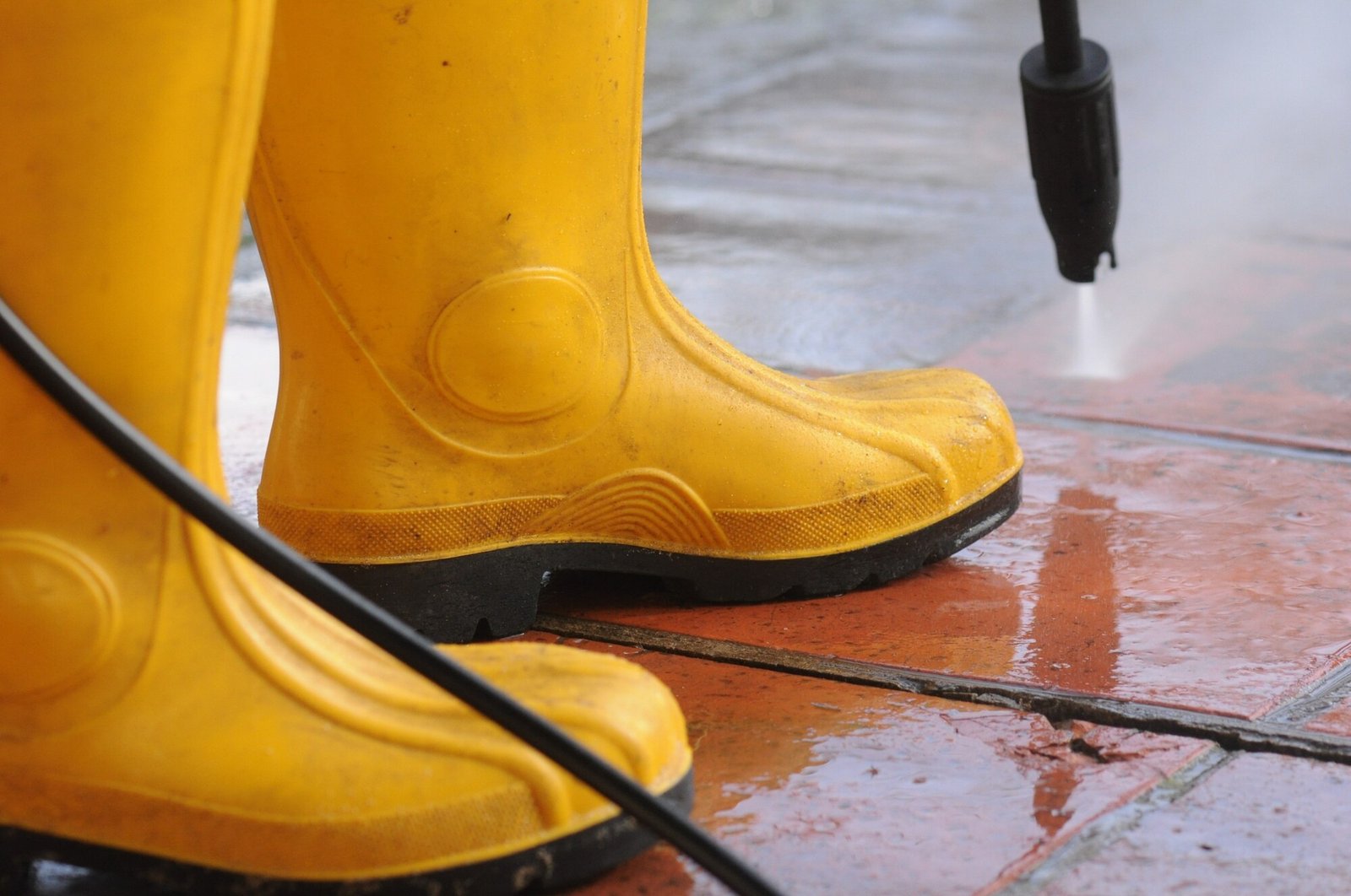 person-wearing-yellow-rubber-boots-with-high-pressure-water-nozzle-cleaning-dirt-tiles_181624-24808